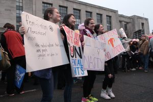 Four young women pose for a photo holding their signs for the Women's March. Photo by Lu Gerdemann.